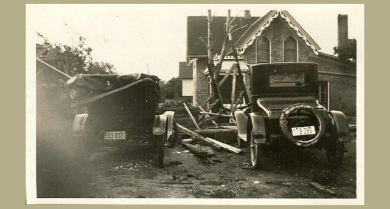 Two cars in front of a house with debris in the yard