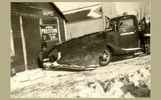 Person sitting in front of blade of snow plow from 1939